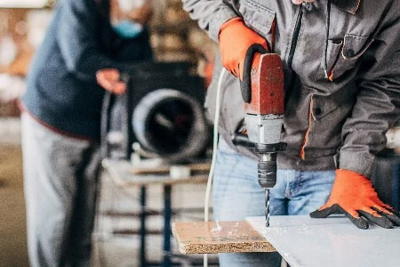 Person bohrt mit Bohrmaschine in Platte